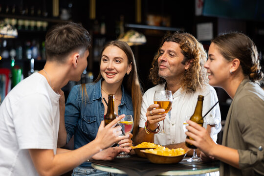 Company of joyful friends drinking beer, eating chips and talking with each other in the sport pub
