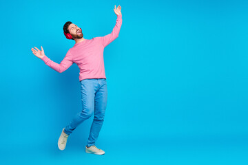 Joyful bearded man dancing with headphones in stylish pink and blue outfit against vibrant blue background