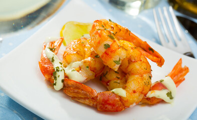 Grilled shrimps served with herbs, garlic sauce and lemon on white plate