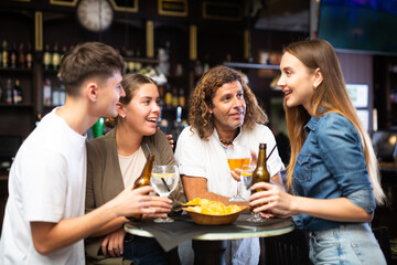 Group of friends standing at table in bar, drinking beer and having conversation.
