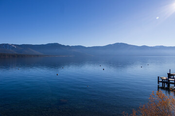 a gorgeous winter landscape at Lake Tahoe with blue lake water, lush green trees and plants,...