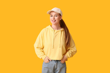 Happy young woman in stylish white cap on yellow background