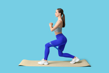 Young female trainer training with elastic band on blue background