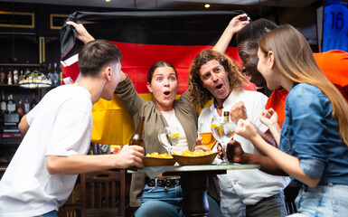 Group of emotional friends, football fans, having fun in sports bar, cheering for favorite German team together while watching match