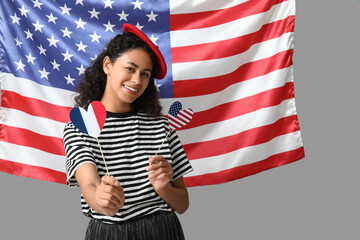 Beautiful young happy African-American woman with USA and France flags in shape of hearts on grey...