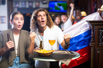 Man and woman, Russia football team fans, spending time in bar, drinking bear and screaming chants. People with state flag in pub.