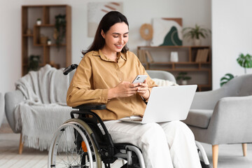 Young woman in wheelchair using laptop and mobile phone at home