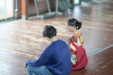 A Japanese woman in her 20s wearing a red hakama, a staple for Japanese university graduates, and a teenage man wearing casual clothes are sitting in a room.