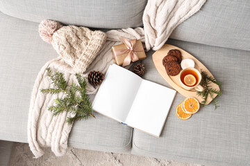 Blank book with winter accessories, Christmas gift and tea on sofa, top view