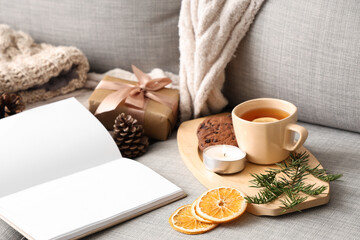 Book with tea and burning candle on sofa, closeup