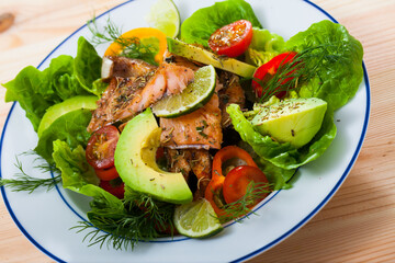 Close up of tasty salad of fried trout, avocado, tomatoes and greens
