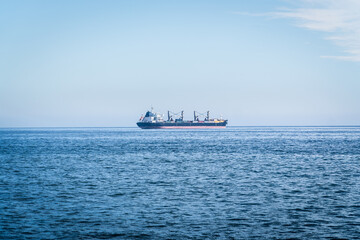 A large container cargo ship travels over calm, blue ocean