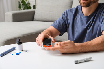 Diabetic young man using glucometer at table in room, closeup