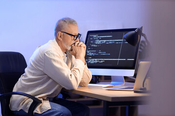 Thoughtful mature programmer working in office at night