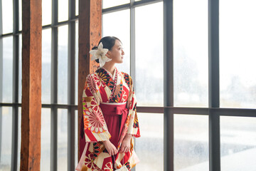 A Japanese woman in her 20s, wearing a red kimono (Hakama), a staple of Japanese university graduates, stands in a clean glass room, looking a little lonely.