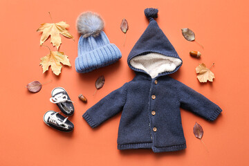 Composition with stylish baby clothes, shoes and fallen leaves on color background