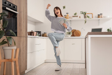 Happy young woman with dollar banknotes in kitchen