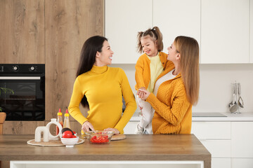 Young lesbian couple with their little daughter cooking in kitchen