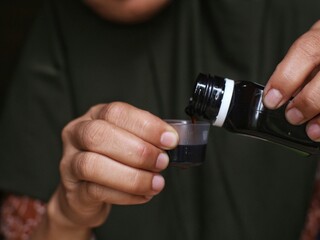 A mother pours flu cough syrup into her child's dosage container