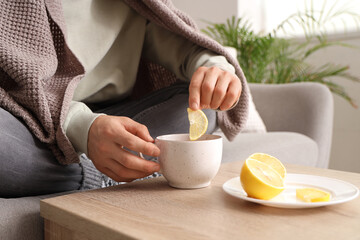 Ill young man putting lemon slice into cup of tea at home, closeup