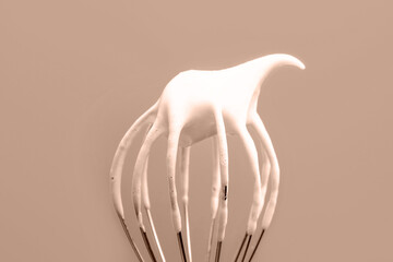 Whisk with whipped cream from proteins close-up against the backdrop of the trendy color of 2025.