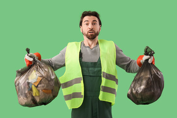 Shocked male scavenger with full garbage bags on green background