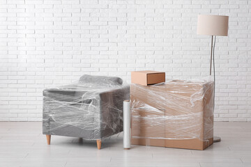Wrapped armchair and cardboard boxes with stretch film in room on moving day