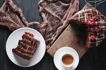 A slice of cake with chocolate and cherry on a plate. Cup of espresso and cake on a wooden board. Top view.