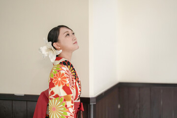 A Japanese woman in her 20s stands indoors wearing a red kimono (hakama), a staple for Japanese university graduates.