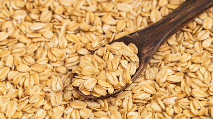 Rustic wooden spoon filled with rolled oats on a background of scattered oats. Ideal for themes of healthy eating and organic food.