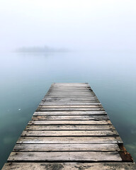 Fototapeta premium A serene wooden dock extending into a foggy lake, creating a tranquil atmosphere.