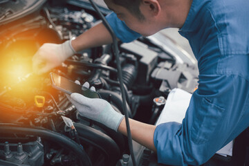 Smiling technician taking a break at car workshop, texting on mobile phone. Close-up shot of...