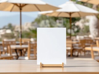 Blank menu booklet mockup on wooden table outdoors cafe. Empty white booklet on stand. Blurred background shows cafe tables with chairs, umbrellas. Ideal for restaurant marketing. Outdoor cafe