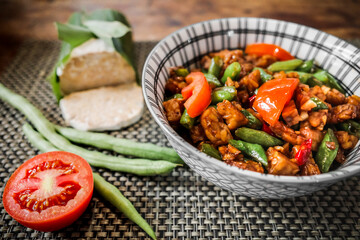 Delicious Indonesian lunch menu of stir fry tempeh and string beans served in a bowl on dining table with raw ingredients on the side