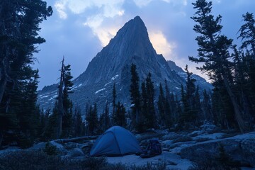 A serene campsite near a towering mountain, surrounded by trees at dusk.