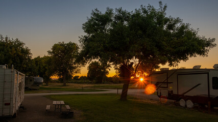 Rv camping at sunset with sunburst trees on grass in low light 