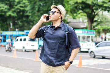 Traveler Asian Man Wear Sunglasses Calling Using Smartphone While Looking Away on City Street