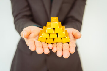 Close-up of a businessman holding shiny gold bars, symbolizing wealth and investment, isolated on a...