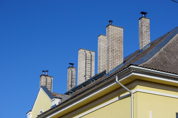 Obraz premium The roof of a yellow building with many white brick chimneys on a blue sky background