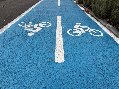 Bicycle sign on a bike path. Empty bike path with a white bicycle icon on a blue background. White bicycle symbol drawn on the rubber separating the cycling lane for bikers in the park. No models.
