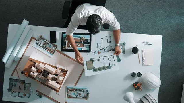 Top view of business man using tablet plan house design while sitting at meeting table with blueprint and equipment scatter around. Aerial view of civil engineer working at blueprint. Alimentation.