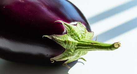 Obraz premium A close-up of an eggplant's glossy purple body and vibrant green stem on a clean white surface
