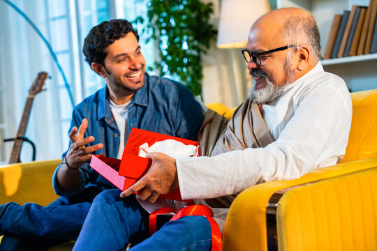 Indian Asian Senior father, young son bond over an emotional gift on a sofa in a modern home - Powered by Adobe