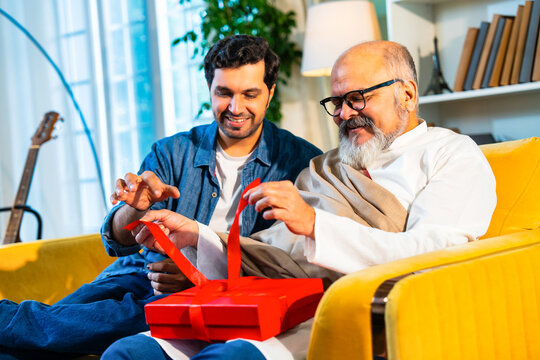 Indian Asian Senior father, young son bond over an emotional gift on a sofa in a modern home - Powered by Adobe