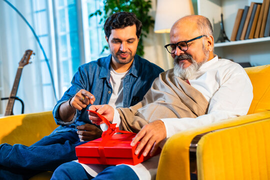 Indian Asian Senior father, young son bond over an emotional gift on a sofa in a modern home - Powered by Adobe