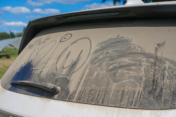 dust and dirt on the rear window of a car with funny drawings