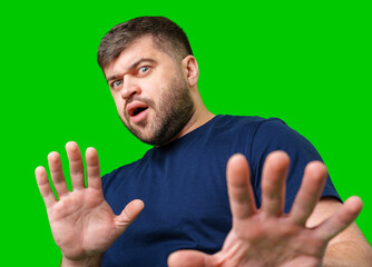 A man with a serious expression holds up both hands in a stopping gesture against a bright green...