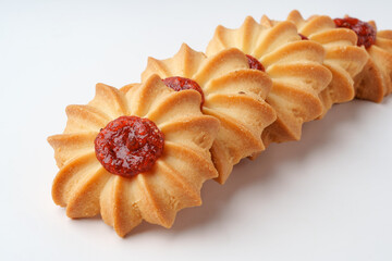 Sweet cookie blossoms topped with red fruit preserves arranged in a decorative pattern on a white...