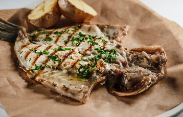 sea bream fish fillet seasoned with sauce, mediterranean herbs, served with baked potatoes on parchment cooking paper and plate