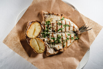 sea bream fish fillet seasoned with sauce, mediterranean herbs, served with baked potatoes on...